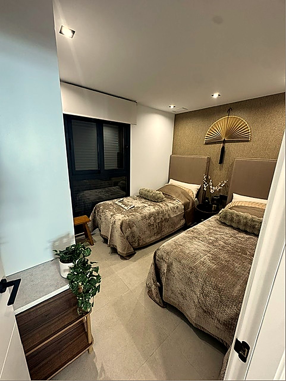 Slaapkamer met twee losse bedden en een goudkleurige waaier aan de muur